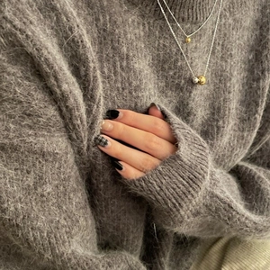 Minimalist double-layer necklace with golden and silver beads worn on a grey sweater