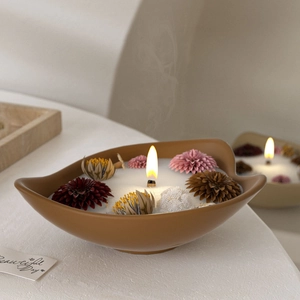 Macro shot of ceramic candle bowl featuring dried flower decor and a burning wooden wick