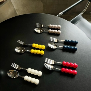 Modern stainless steel fork and spoon set with colorful beaded ceramic handles on a black table