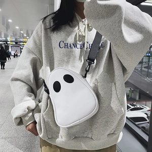 Ghost-shaped white PU crossbody bag with large black eyes shown on model in public station