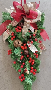 Close-up of handmade Christmas teardrop swag with red berries, ribbons and rustic bells
