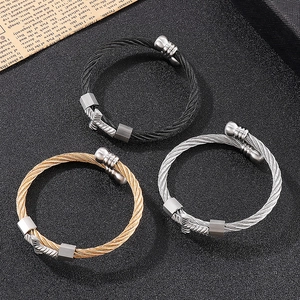 Detailed view of woven steel cable bracelets in black, gold, and silver with cross charms