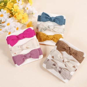 Three-pack of baby muslin bow headbands with soft pleated texture on a display card