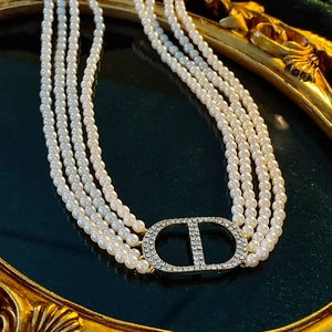 Detail of layered pearl necklace featuring a diamond-encrusted CD logo in a golden frame