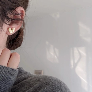 Close-up of a textured gold heart stud earring on a model in a minimalist setting
