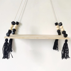 Detail of wooden wall shelf with macaron beads and black tassel decor in Nordic style