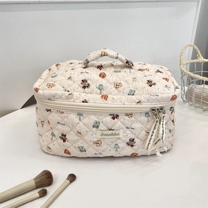 Detail view of quilted beige makeup bag with cartoon bear patterns and decorative ribbons