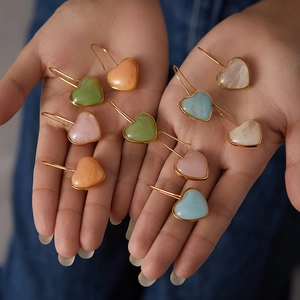 Close-up of heart-shaped resin earrings in five colors with gold trim held by hand