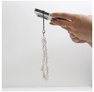 Détail de la dragonne de téléphone en cristaux roses et perles blanches tenue à la main