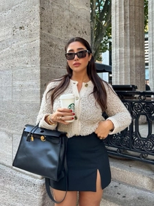 Streetstyle look met crèmekleurig gebreid vest, zwarte rok en een chique handtas