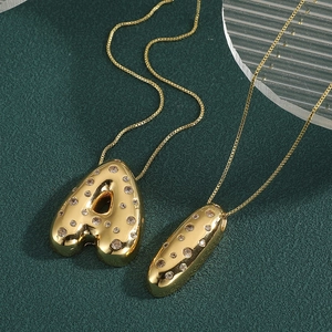 Detailed view of 18k gold plated A letter pendant with cubic zirconia on green background