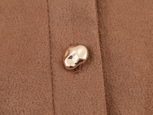 Detailed close-up of brown knit fabric texture with an irregular golden metal button