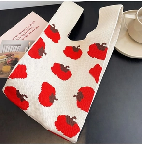 Macro shot of beige knitted tote bag with red persimmon patterns and sturdy top handle