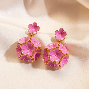 Gros plan détaillé des boucles d'oreilles fleurs en émail rose sur fond de soie champagne
