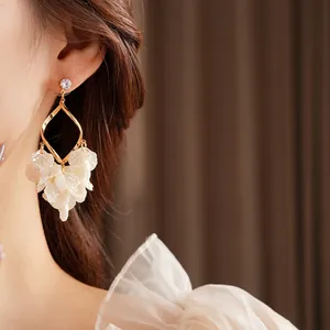 Elegante goldene geometrische Ohrringe mit weißen Muschelquasten an einem weiblichen Model