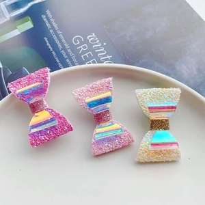 Three glittering bow hair clips in pink and yellow on a white ceramic tray detail