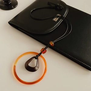 Detail of vintage necklace with orange resin ring and dark brown pendant on black bag
