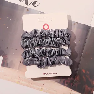 Macro shot of 4-pack grey satin hair scrunchies on a professional display card