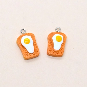 Detailed macro view of two resin toast and fried egg pendants with metal rings