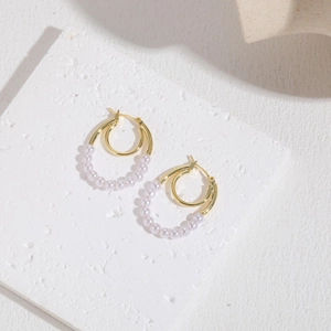 Elegant double hoop gold earrings with delicate white pearls on a stone pedestal