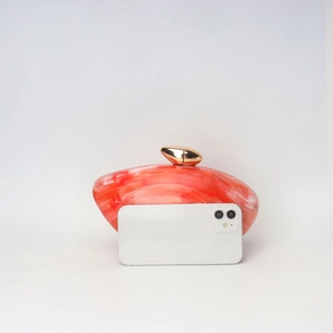 Red marble acrylic clutch bag with gold buckle shown next to a smartphone for scale