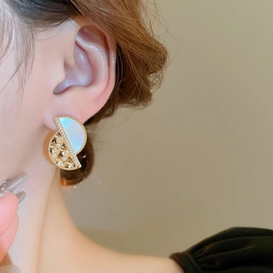 Macro shot of semi-circular gold earrings with mother-of-pearl and zircon on model ear