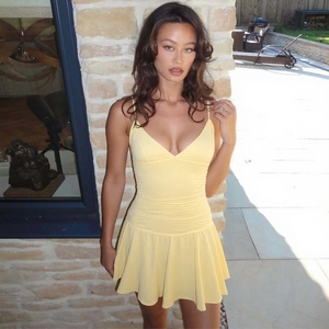 Detail of yellow V-neck sundress featuring ruched waist and ruffled hemline in sunlight