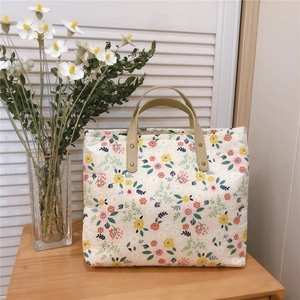 Floral print canvas tote bag with leather handles on a wooden table with daisies