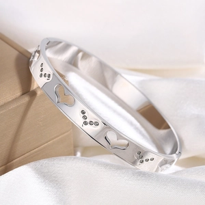 Detailed close-up of silver hollow heart bracelet with diamonds on silk background