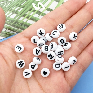 Detailed view of hand holding white round alphabet beads with black letters and symbols
