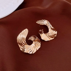 Detail of gold metal earrings with spiral shell texture on dark silk fabric