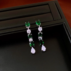Detailed view of silver drop earrings with emerald stones and zircon accents in a box