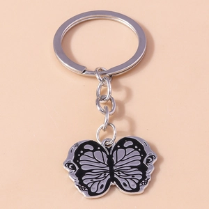 Detail of silver butterfly keychain with black and white enamel wings on beige background