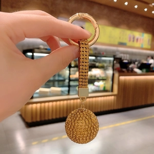 Close-up of sparkling gold crystal ball keychain with diamond bow held in hand