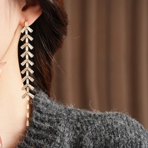 Detailed view of gold tassel earrings with leaf-shaped cubic zirconia on model