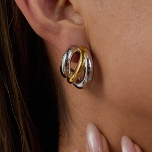 Close-up of model wearing two-tone gold and silver stainless steel oval hoop earrings
