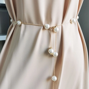 Close-up of elegant pearl waist chain with gold links and tassel on champagne dress