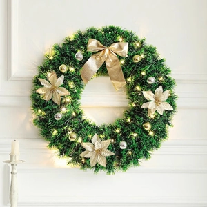 Green Christmas wreath with gold bow, red flowers, and LED lights on a white wall