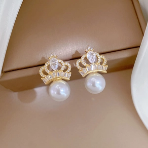 Macro shot of crown earrings with white pearls and sparkling crystals in gold finish