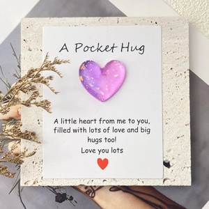 Macro shot of purple gradient resin heart with Pocket Hug greeting card on stone background