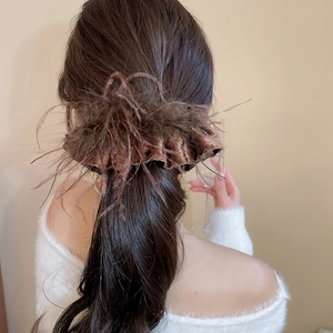 Detail of luxury feather tassel hair clip with brown satin texture on a ponytail