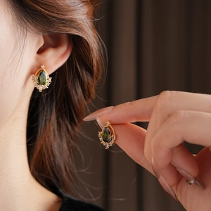 Dettaglio di orecchini vintage in oro con pietre verdi a goccia e zirconi sulla modella