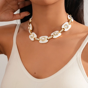 Gros plan d'un collier doré avec maillons ovales en émail blanc et cristaux incrustés
