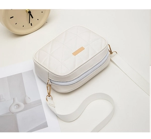 Detail of white quilted crossbody bag featuring gold hardware and a wide fabric strap