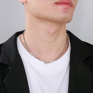 Close-up of a silver rectangular link chain necklace worn by a model in a minimalist style