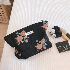 Detailed embroidery view of floral pattern on black fabric cosmetic bag with zipper