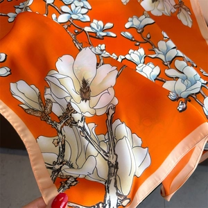 Close-up of magnolia print on orange silk scarf showing smooth fabric texture and hem
