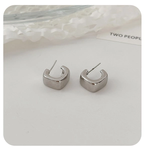 Detailed macro view of square silver metallic C-shape hoop earrings on a minimalist white prop