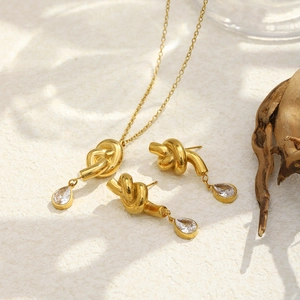 Detailed macro view of 18K gold-plated knotted drop necklace and teardrop zircon earrings