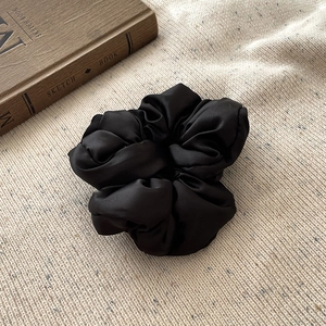Détail d'un chouchou en satin noir sur tissu en maille beige avec livre déco